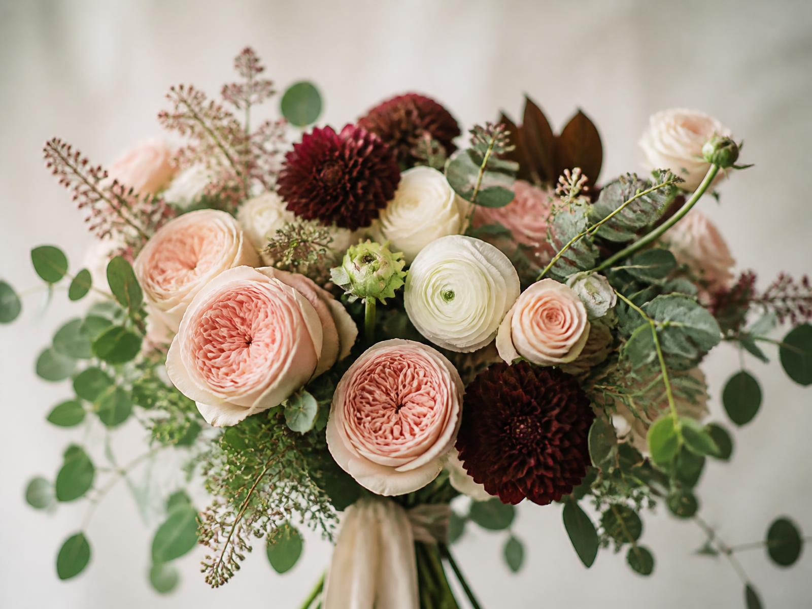 A hand-tied bouquet of blush roses, ivory ranunculus and eucalyptus